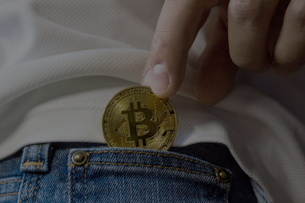 A hand putting a bitcoin in the pocket of a jeans pocket
